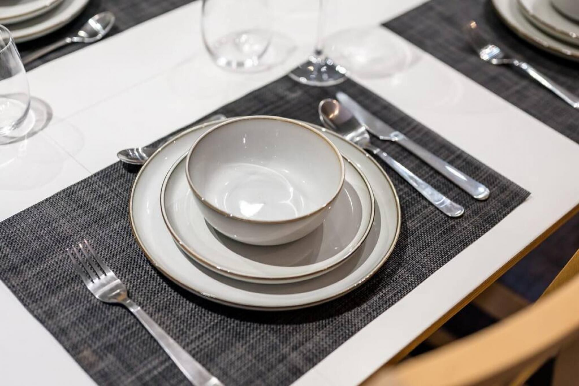 A table set with plates, bowls, cutlery, and wine glasses, indicating a formal dining arrangement.