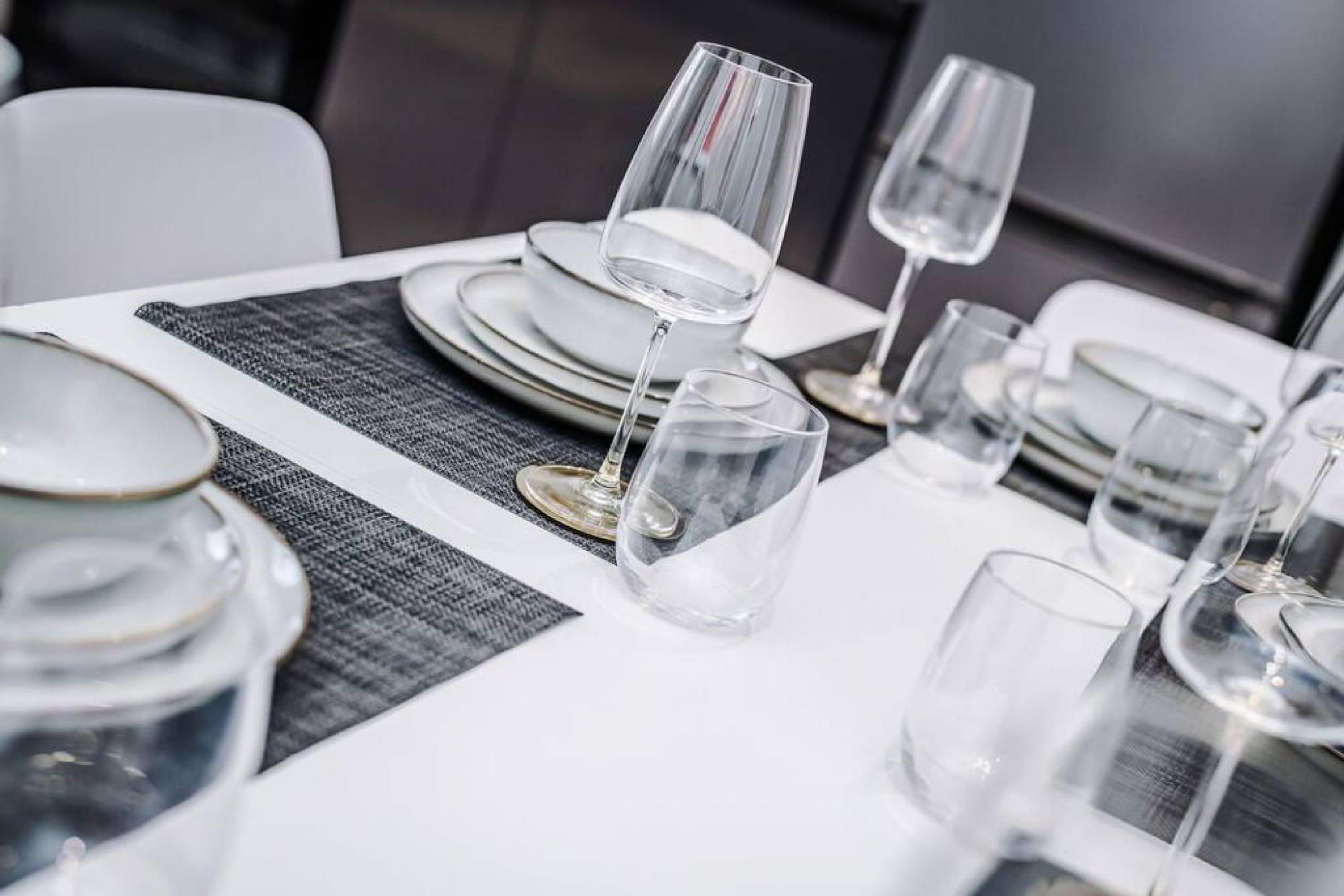 A dining table set with white plates, clear glasses, and a woven placemat.