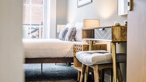 A bedroom with a bed, bedside table, lamp, and a view of a balcony.