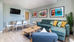 A modern living room with a green sofa, a dining table with chairs, and framed artwork on the walls.