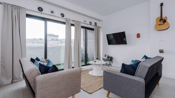 Een moderne woonkamer met twee banken, een salontafel, een aan de muur bevestigde televisie en een gitaar.