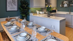 A modern kitchen with white cabinets, a central island with a sink, and a dining area set for six with plates, glasses, and cutlery. - Host Apartments The Falkner Quarters III (Liverpool)