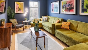 A modern living room with a green sofa, a wooden coffee table, and a small side table. There are framed pictures on the wall and a large window providing natural light. - Host Apartments The Falkner Quarters III (Liverpool)