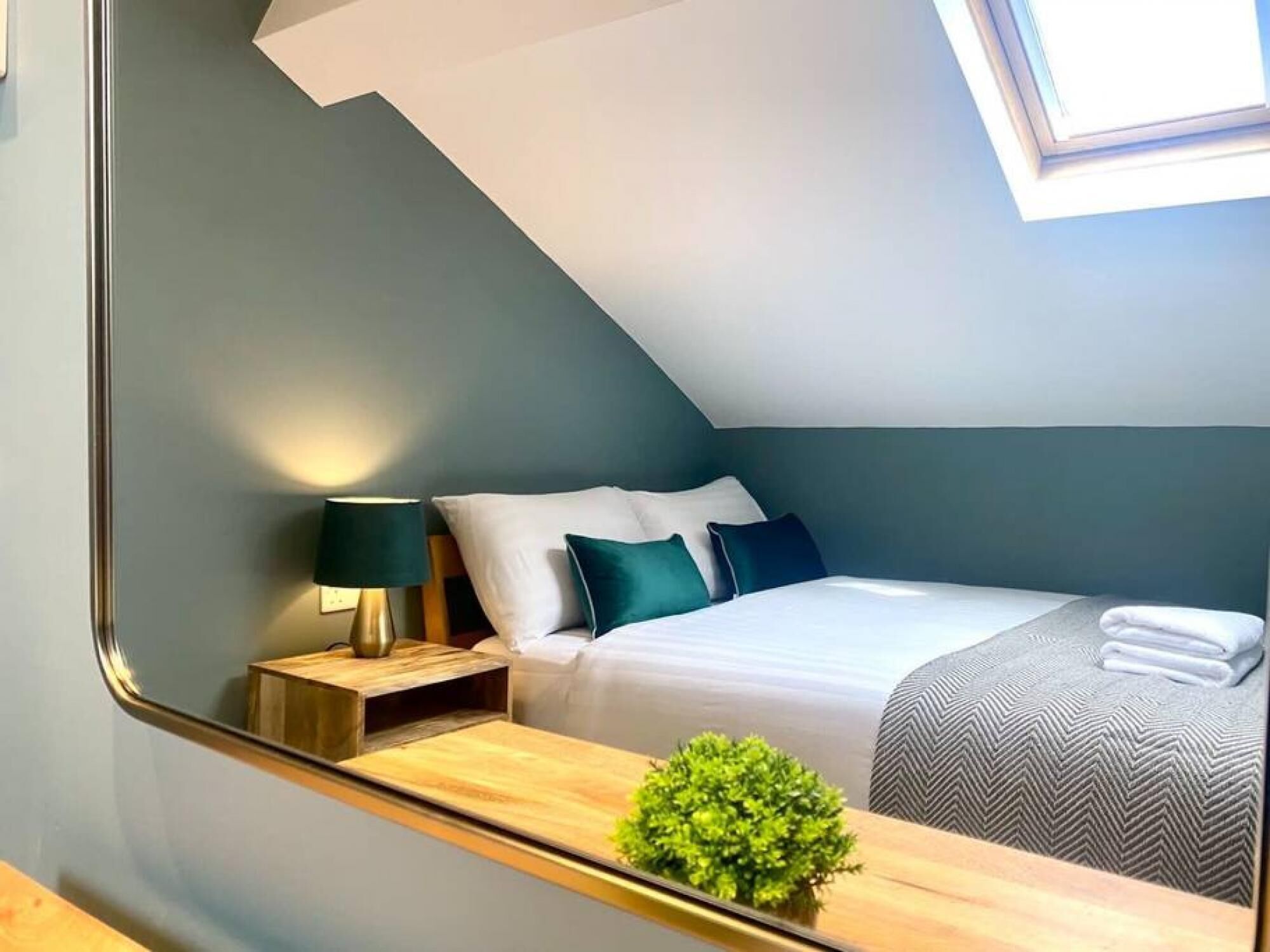 Une chambre à coucher moderne avec une lucarne, un lit soigneusement fait, une table de chevet avec une lampe et une petite plante en pot.
