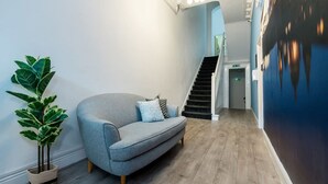 A modern interior with a grey sofa, a potted plant, and a staircase leading to an upper level. - Host Apartments The Georgian Quarters at Canning (Liverpool)