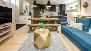 Ein modernes Wohnzimmer mit einem blauen Sofa, einem Holztisch und einem Fernseher auf einem Holzständer.