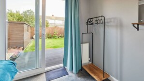 A room with a sliding glass door leading to a garden, a metal drying rack, and a small wooden shelf. - Host Stay Sands Walk Cottage (Redcar)