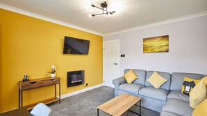 A living room with a sofa, a coffee table, a TV, and a console table with a vase. - Host Stay Sands Walk Cottage (Redcar)