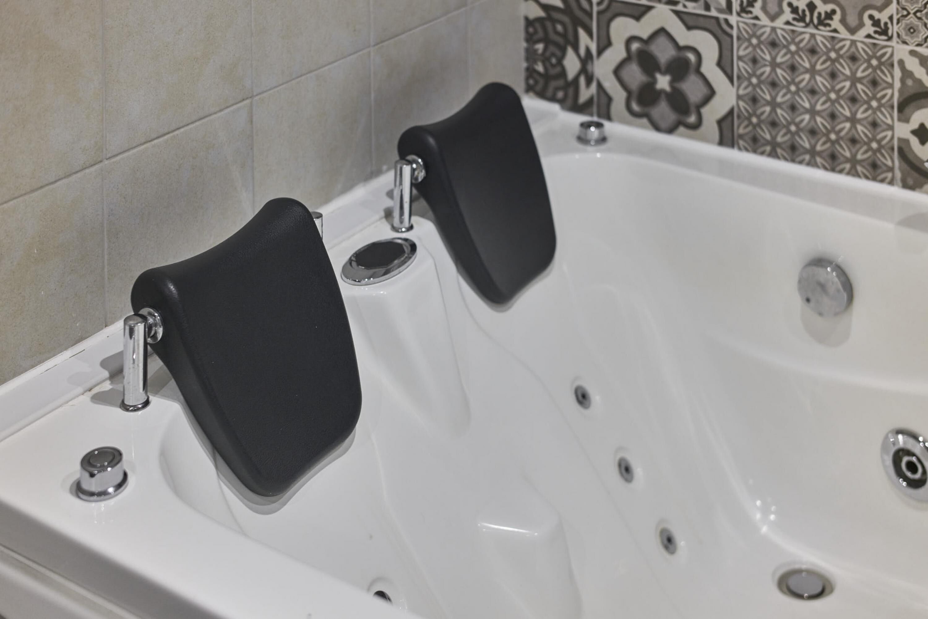 A white bathtub with two black non-slip mats, a chrome faucet, and a single drain.