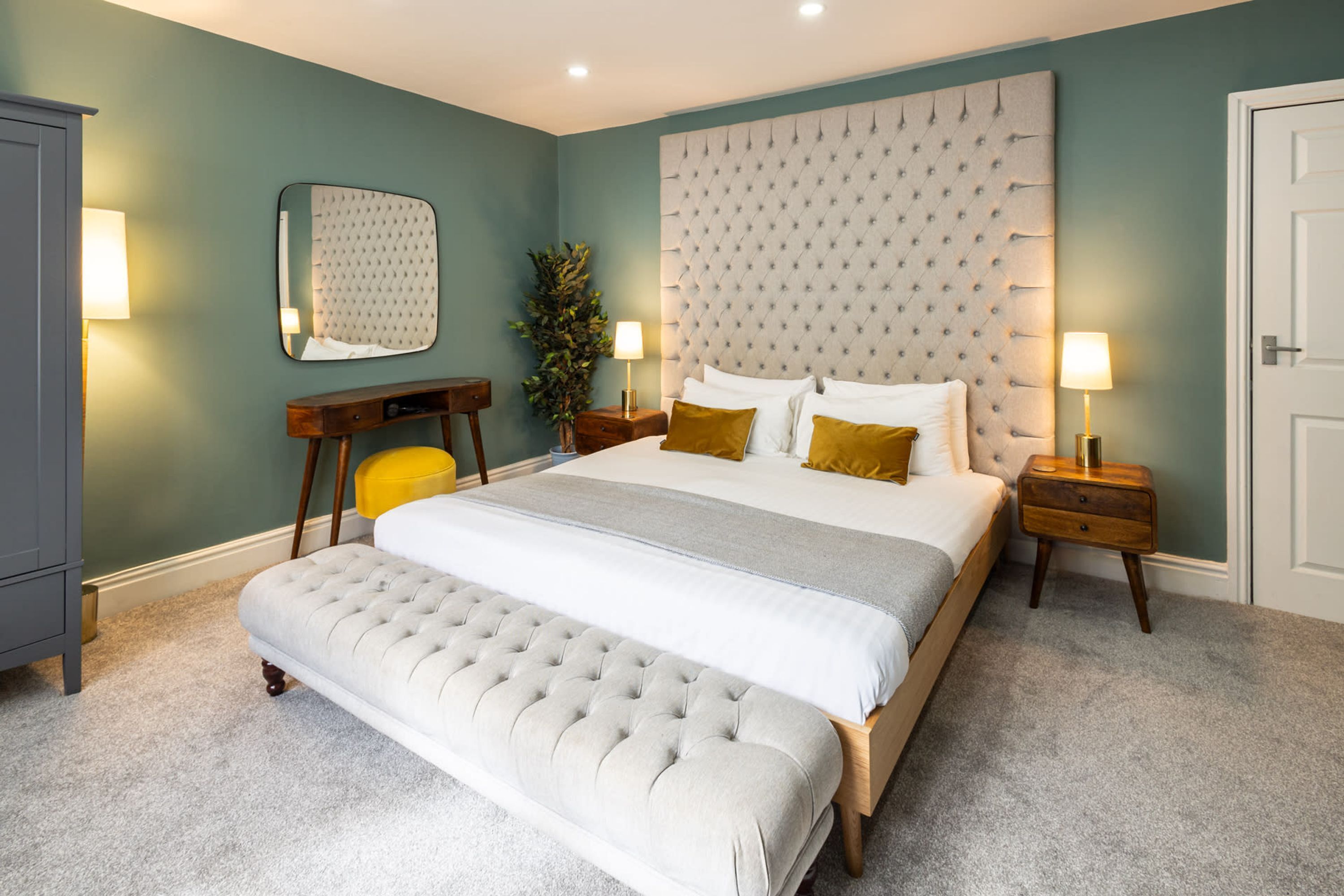 A bedroom with a large bed, a bedside table, a nightstand, a mirror, and a wardrobe.