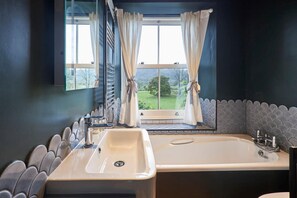 Une salle de bain avec une grande baignoire, un lavabo et une fenêtre avec des rideaux.