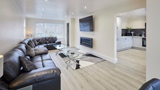 A modern living room with a leather sectional sofa, a glass coffee table, and a flat-screen TV mounted on the wall. - Host Stay Violet s View (Whitby)