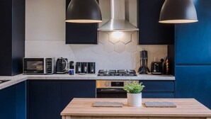 A modern kitchen with dark cabinets, a stainless steel range hood, and pendant lighting. - Host Apartments The Georgian Coach House 2 (Liverpool)