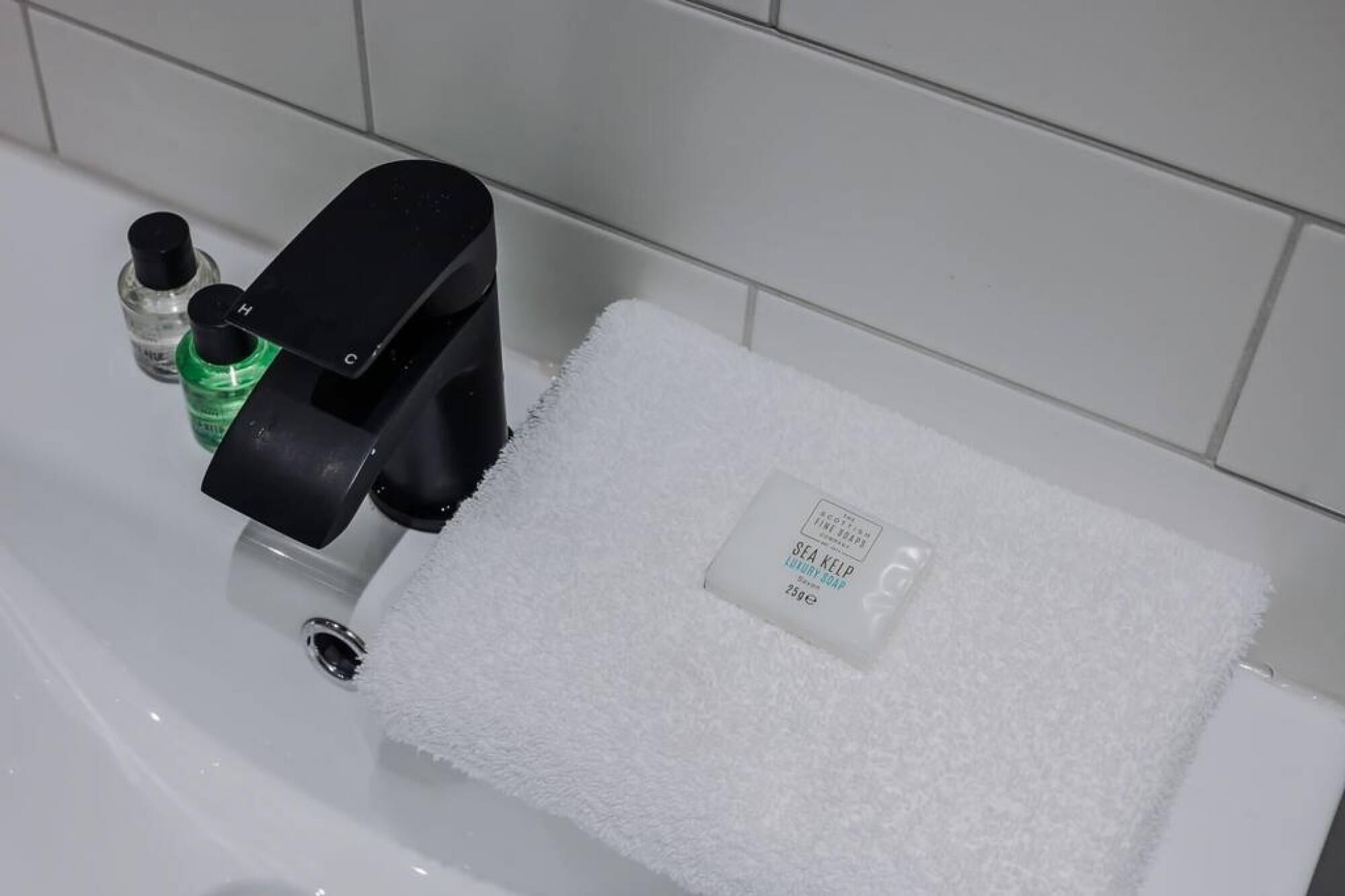 Een badkamer met een wit wastafel, een zwarte zeepdispenser en een groene fles handzeep.