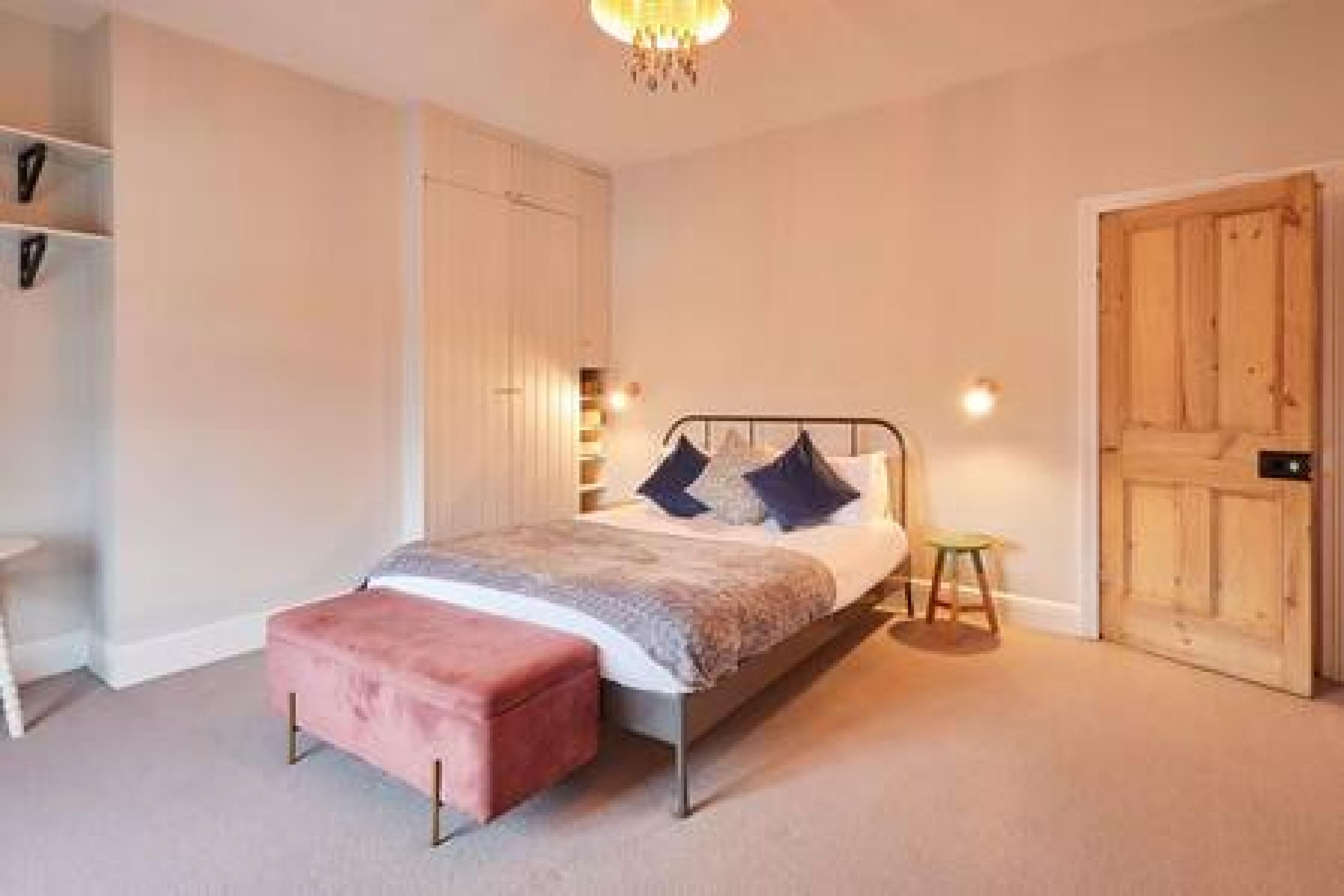 A bedroom with a bed, a wooden wardrobe, a small stool, and a chandelier.