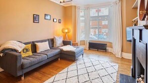 A living room with a grey sofa, a patterned rug, and a radiator. - Host Stay Bath Street (Saltburn-by-the-Sea)