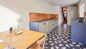 A modern kitchen with a wooden countertop, a dining table with chairs, and a patterned floor. - Host Stay Bath Street (Saltburn-by-the-Sea)