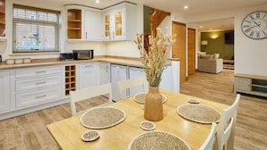 A modern kitchen with white cabinets, a wooden dining table with woven placemats, and a vase with dried flowers. - Host Stay Fawcett Cottage (York)