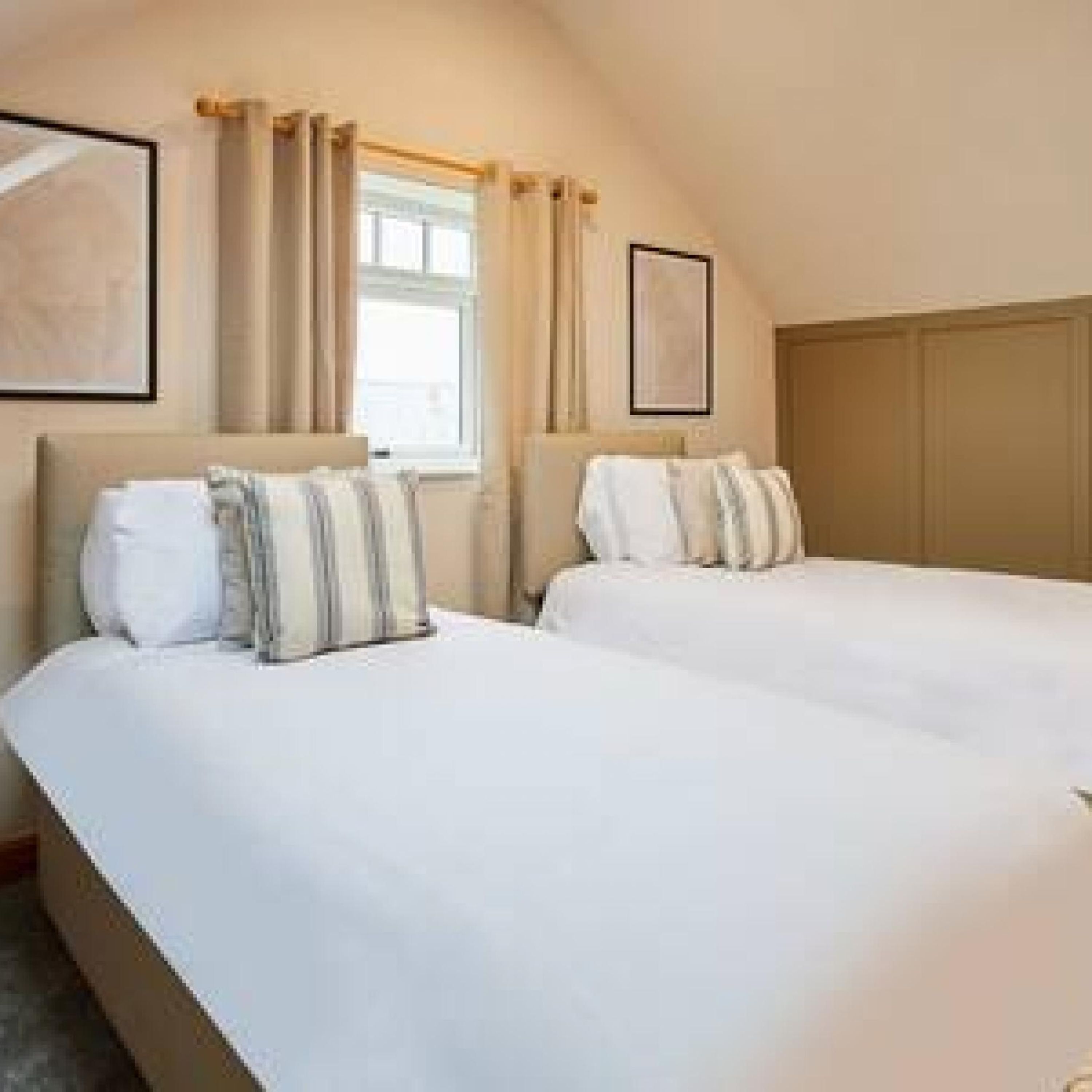 A bedroom with two beds, a window with curtains, and a framed picture on the wall.