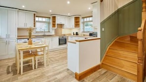 A modern kitchen with white cabinetry, a wooden dining table, and a wooden staircase. - Host Stay Fawcett Cottage (York)