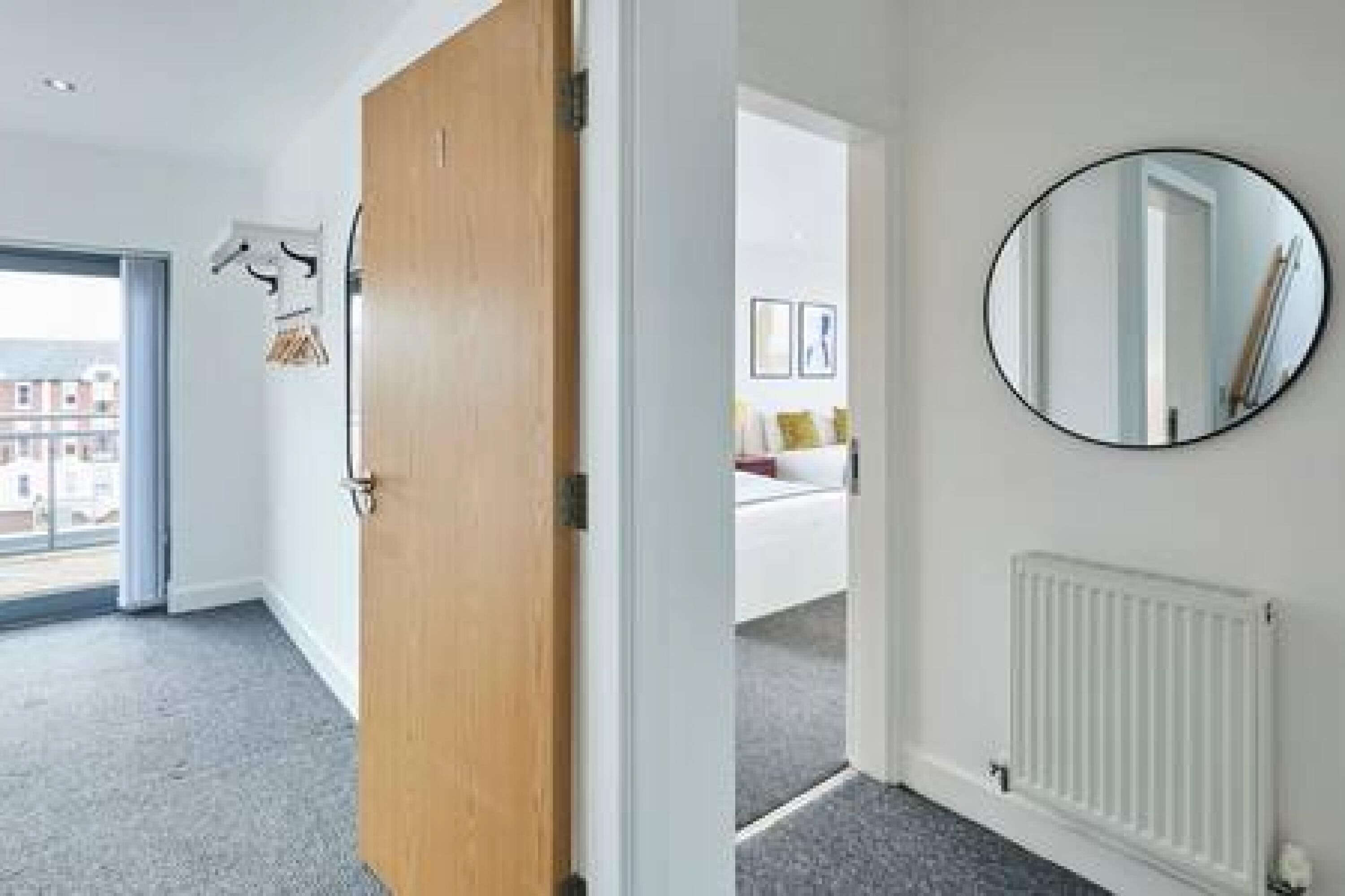 Una habitación con puerta de madera, un espejo redondo en la pared y un radiador blanco.