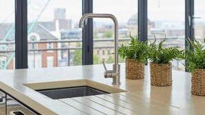 A modern kitchen with a stainless steel sink, a window with a city view, and three potted plants on the counter. - Host Stay The Knight Street Penthouse I (Liverpool)