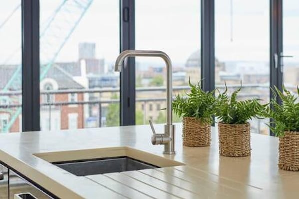 A modern kitchen with a stainless steel sink, a window with a city view, and three potted plants on the counter.