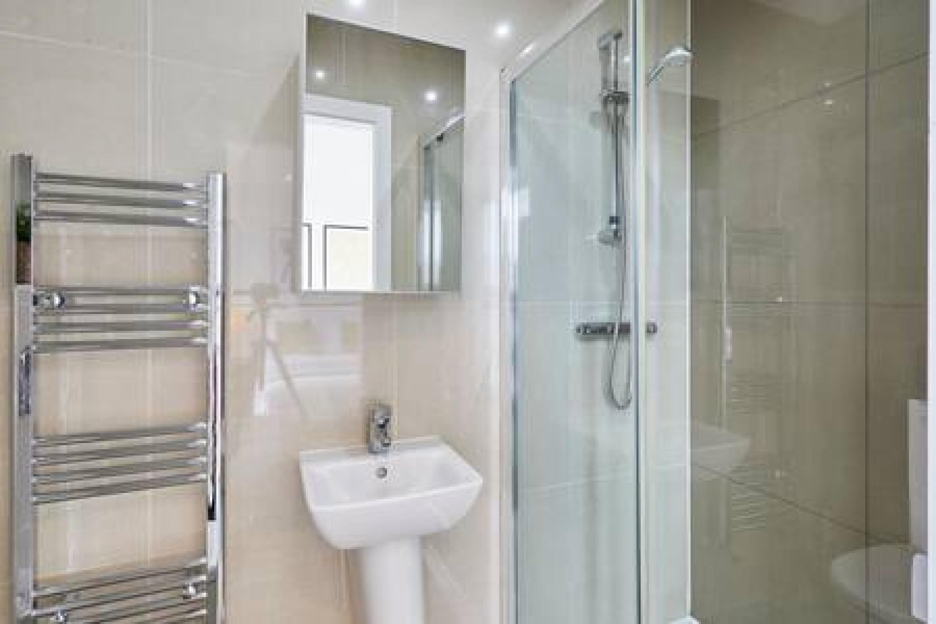 Een moderne badkamer met een glazen douchecabine, een chromen handdoekrek en een witte wastafel.