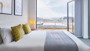 A hotel room with a large bed, a view of the city through a glass door, and framed artwork on the wall. - Host Stay The Knight Street Penthouse I (Liverpool)
