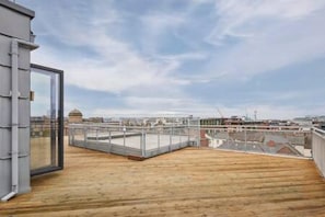 A rooftop terrace with a wooden floor and glass railings.