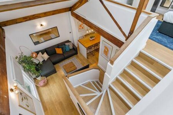 A multi-level interior with a staircase, a living area with a sofa, a small table, and a plant.