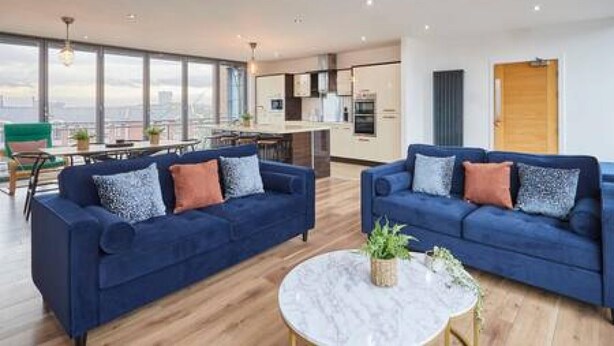 A modern living room with two blue sofas, a round coffee table, and a city view through large windows. - Host Stay The Knight Street Penthouse II (Liverpool)
