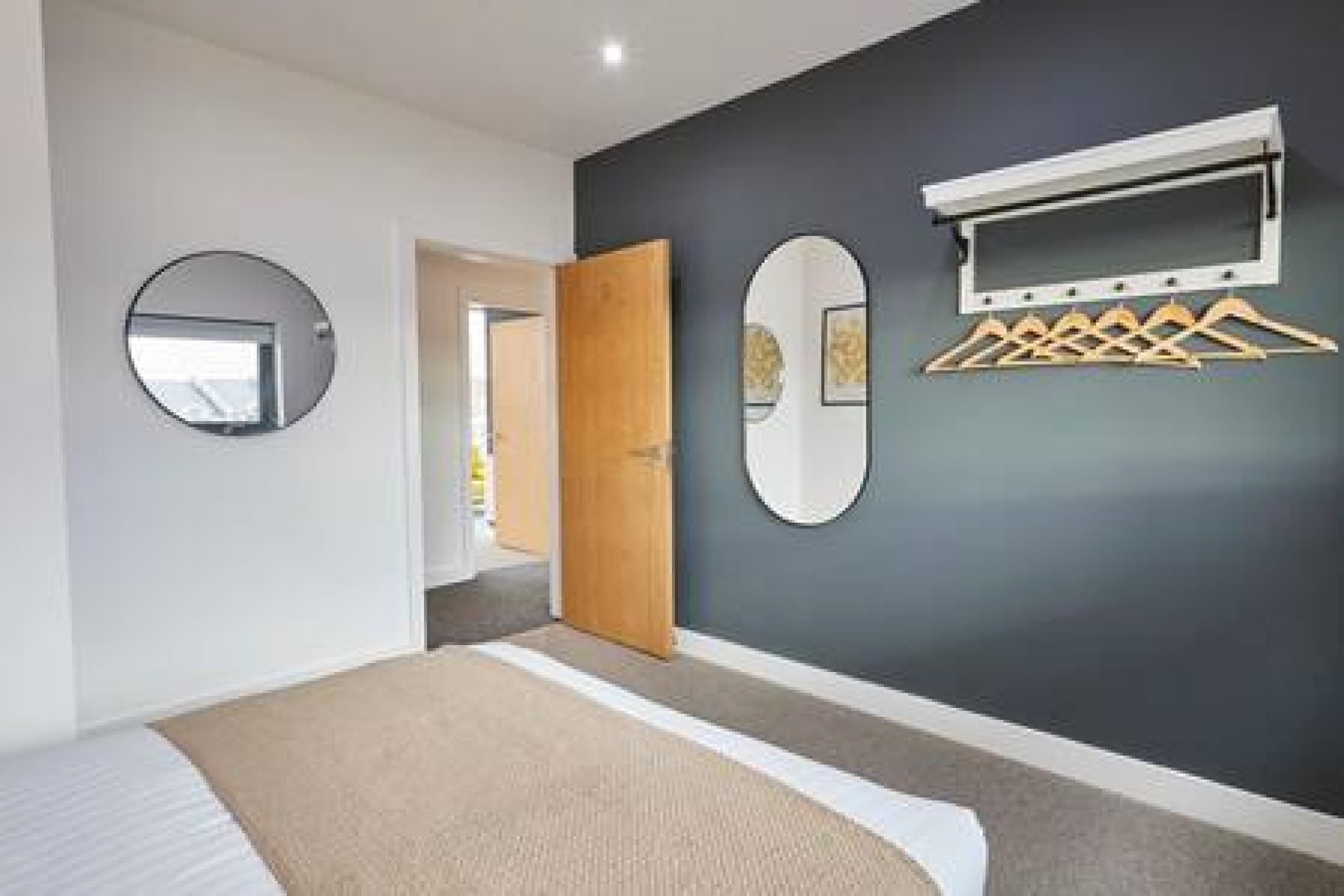 Een slaapkamer met een bed, een ronde spiegel, een houten deur en een wandrek voor wasgoed.