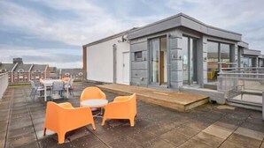 A rooftop terrace with a modern building, outdoor seating, and a clear sky. - Host Stay The Knight Street Penthouse II (Liverpool)