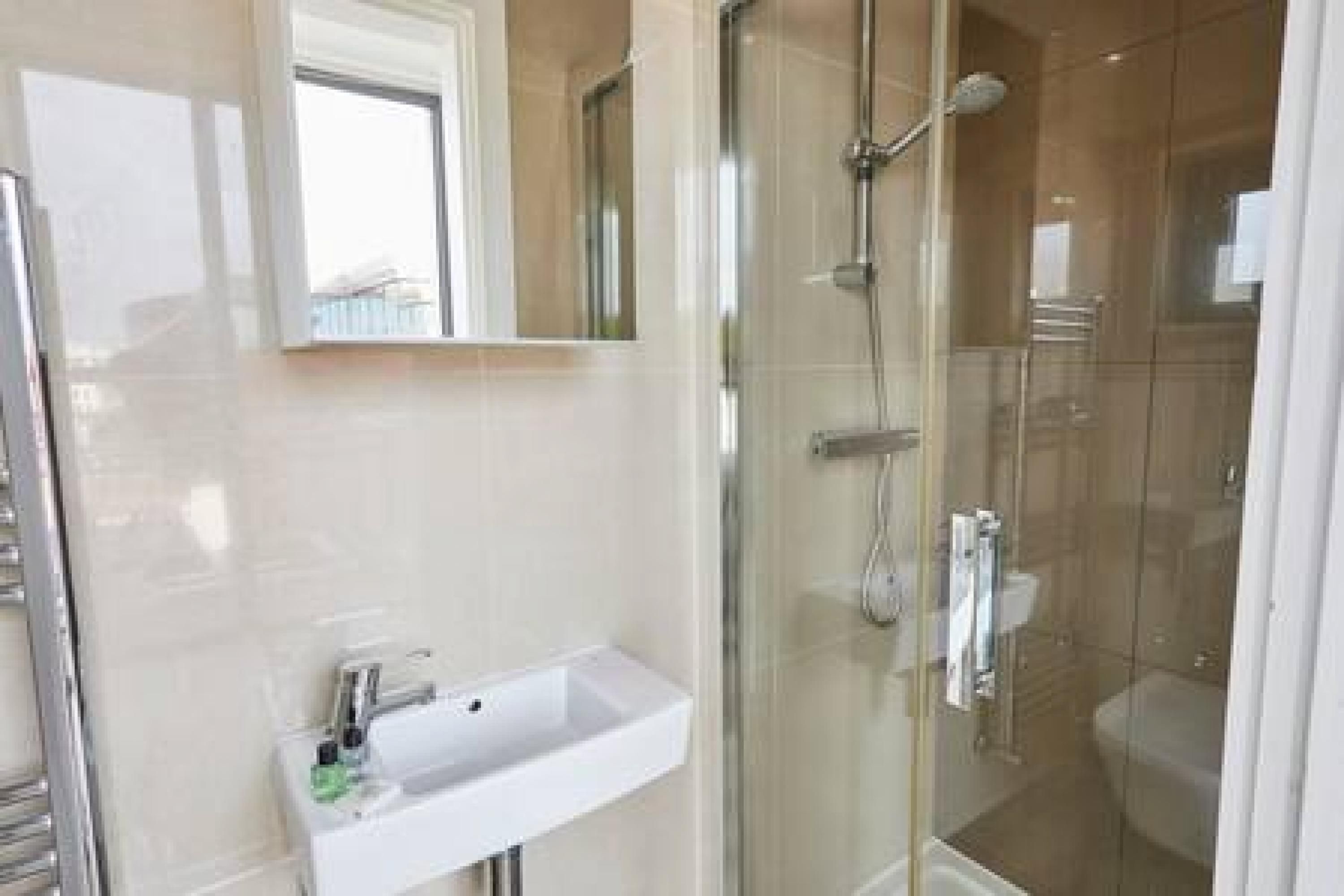A modern bathroom with a glass-enclosed shower, a white sink, and a mirror above it.