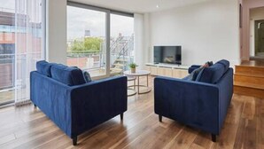 A modern living room with two blue sofas, a small round table, and a TV on a stand. - Host Stay The Knight Street Penthouse II (Liverpool)