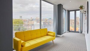 A modern room with a large window, a yellow sofa, and a view of the cityscape. - Host Stay The Knight Street Penthouse II (Liverpool)