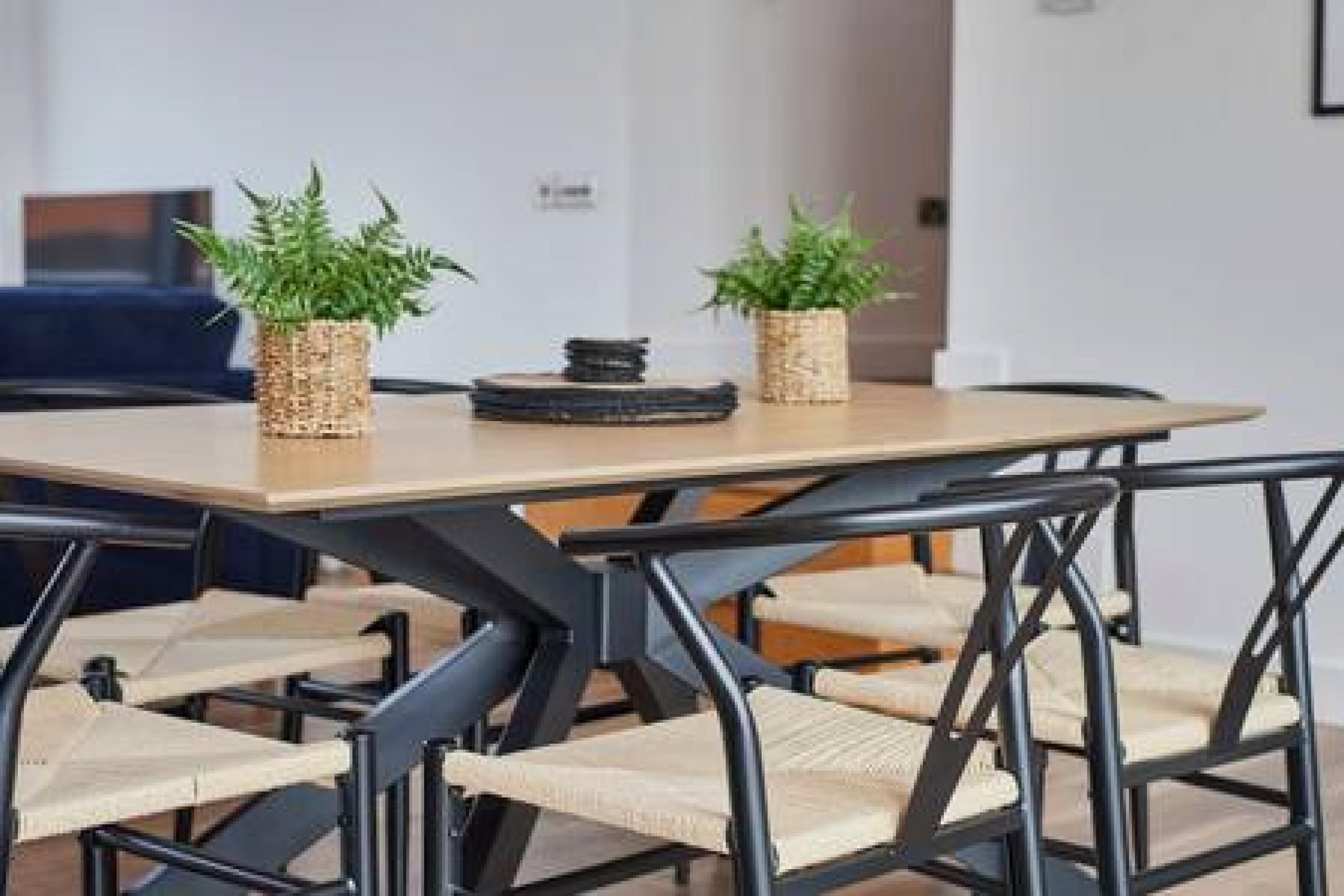 Ein moderner Essbereich mit einem rechteckigen Tisch und schwarzen Metallstühlen. Auf dem Tisch stehen zwei gewebte Körbe mit Grünpflanzen.