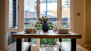 A dining table set with plates, glasses, and a vase, positioned in front of a window with a view of a building and greenery. - Host Stay Ropewalks Quarters III (Liverpool)