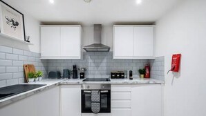 A compact kitchen with white cabinets, a built-in oven, and a tiled backsplash. - Host Stay Halifax House Living (Liverpool)