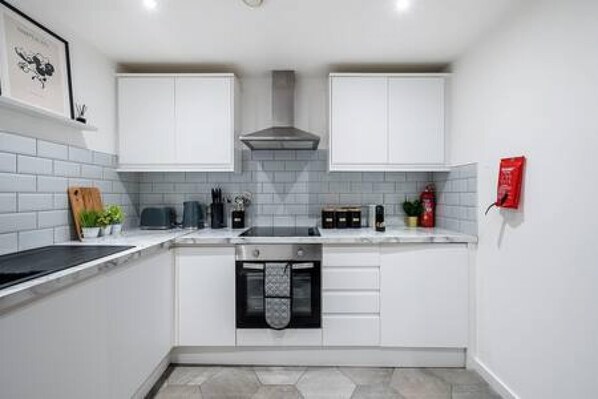A compact kitchen with white cabinets, a built-in oven, and a tiled backsplash.