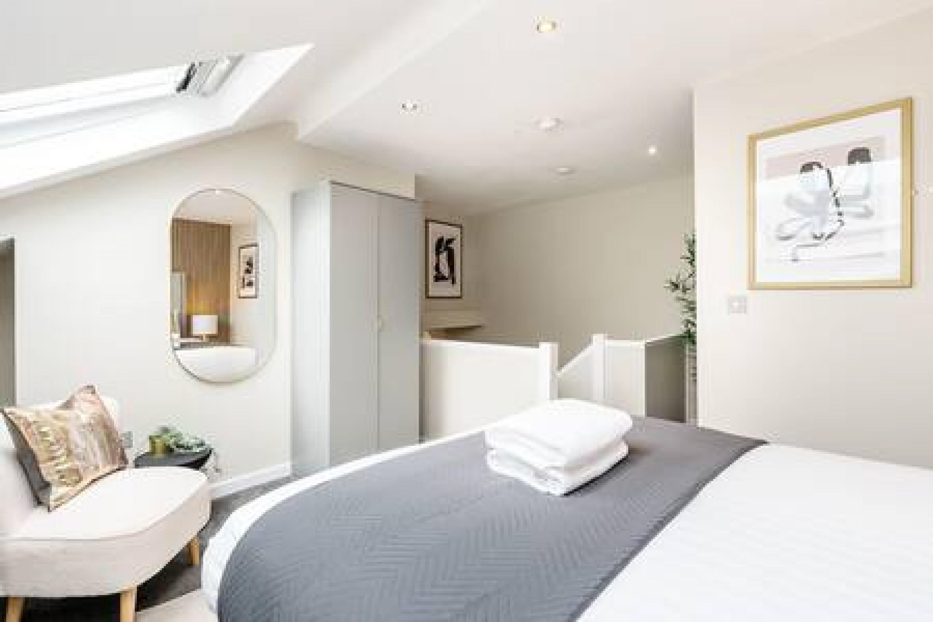 A modern hotel room with a large bed, a bedside table, a chair, and a mirror.
