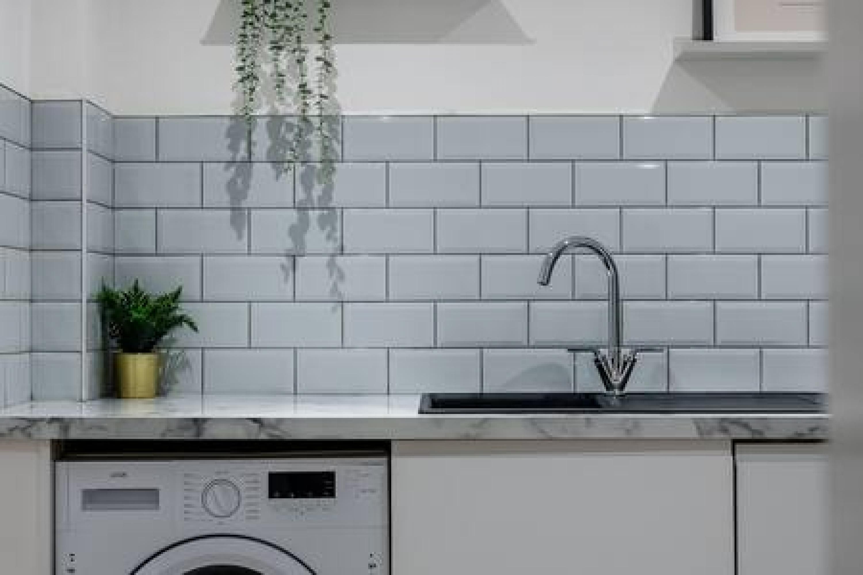 A modern kitchen with white subway tiles, a stainless steel sink, and a built-in washing machine.