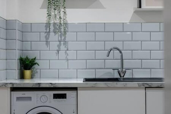 A modern kitchen with white subway tiles, a stainless steel sink, and a built-in washing machine. - Host Stay Halifax House Living (Liverpool)