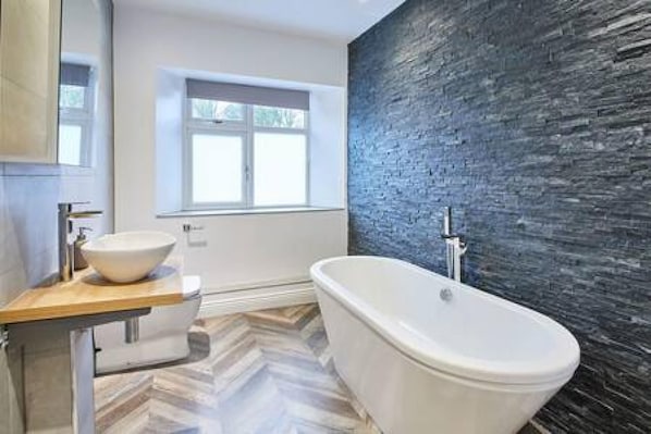 A modern bathroom with a freestanding bathtub, a vessel sink, and a window providing natural light.