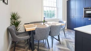 Cocina moderna con comedor, que incluye un ventanal grande, muebles oscuros y suelo de madera en patrón de espiga.