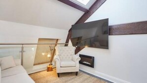 A modern living room with a sofa, a white armchair, a fireplace, and a large TV mounted on the wall. - Host Stay Queen Square Hideaway (Liverpool)