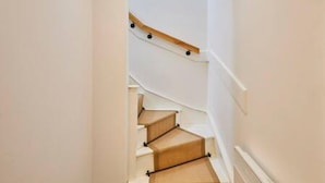 A staircase with wooden steps and black handrails, leading to a landing with a white wall and a light switch. - Host Stay Queen Square Hideaway (Liverpool)