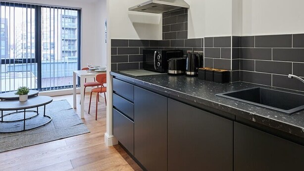 Une cuisine moderne avec un plan de travail noir, une cuisinière encastrée et une grande fen être donnant sur la ville.