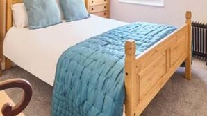 A bedroom with a wooden bed, a nightstand, a window with a view, and a radiator. - Host Stay St Radigunds House (Canterbury)